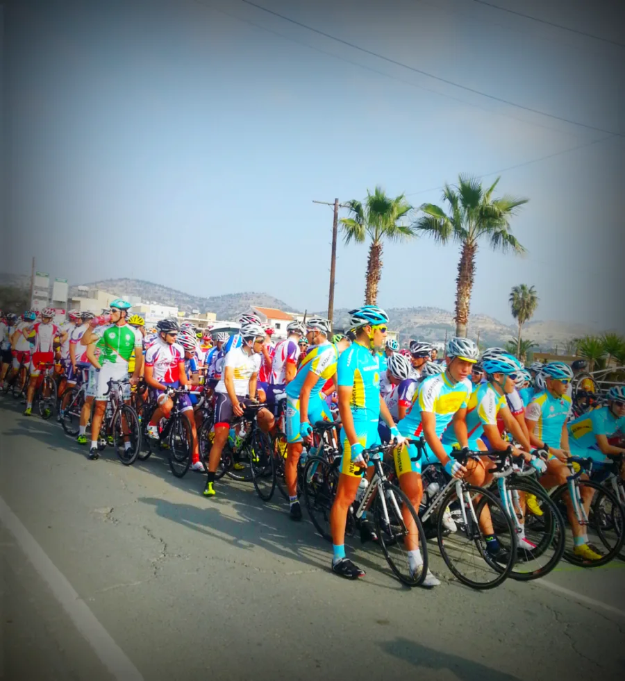 A large bunch of riders waiting at a start line under a row of palm trees