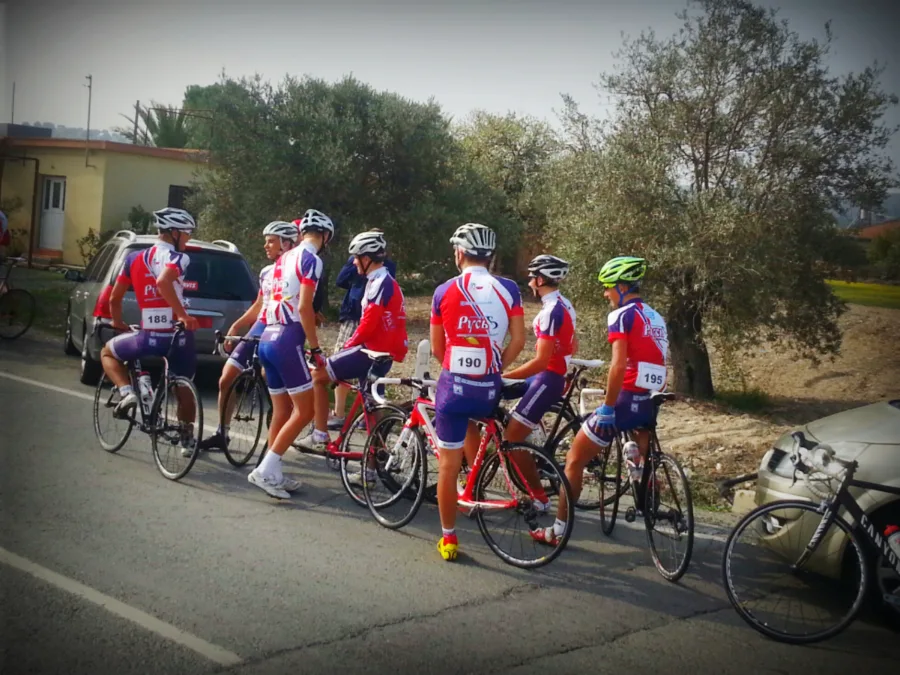 Riders in red and white kit standing over their bikes at a roadside gathering