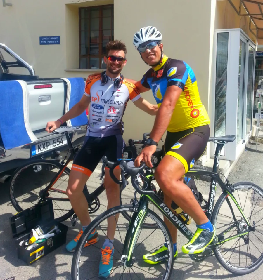 Two riders beside an open support car with a cool box on the tailgate