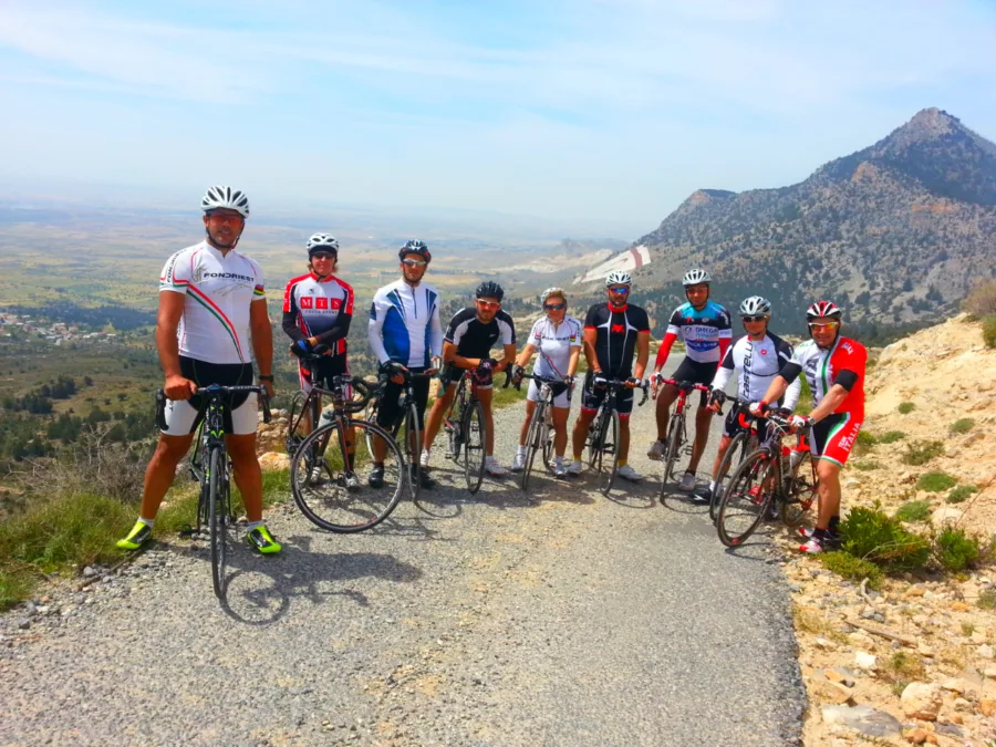 A group of riders with their bikes on a gravel viewpoint below a mountain