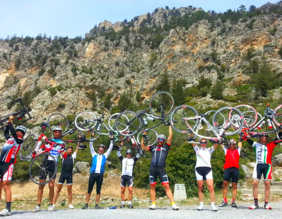 A line of riders holding their bicycles above their heads in front of a rock face