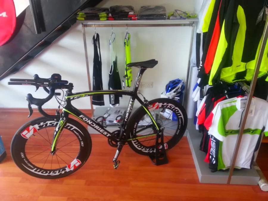 A time-trial bike with deep-section wheels standing in the shop beside racks of clothing
