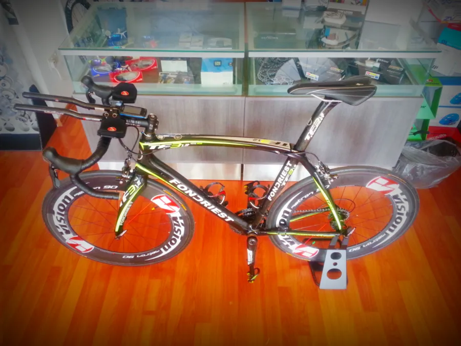A time-trial bike with deep-section wheels indoors on a wooden floor
