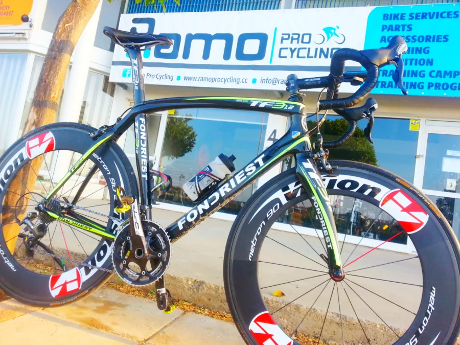A road bike with deep-section wheels standing on the pavement in front of the shop