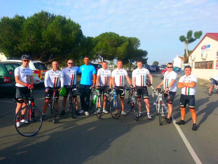 A large group of riders standing with their bikes on a road under trees
