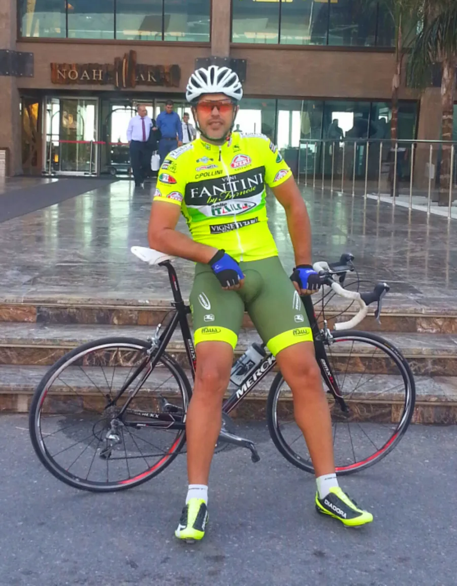 A rider in yellow team kit standing with a road bike outside a building