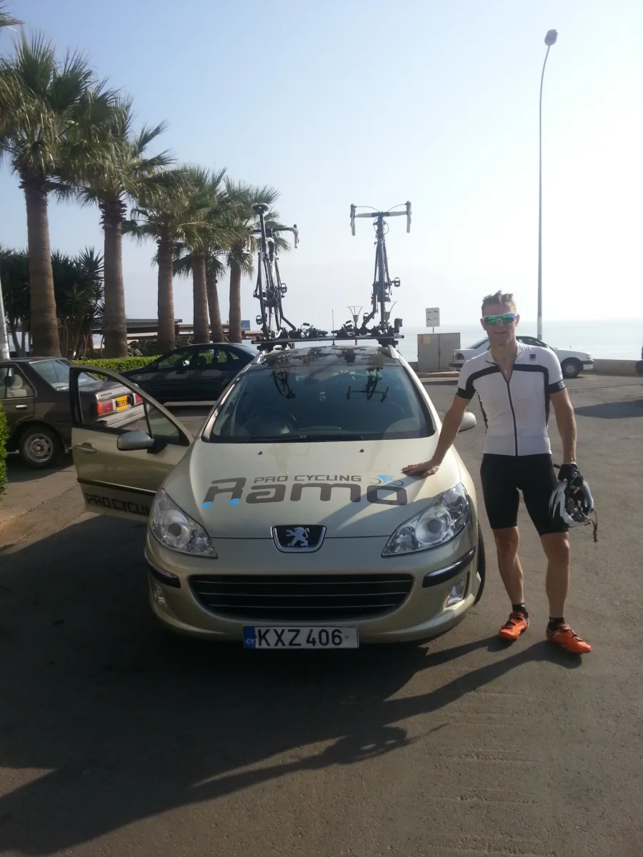 Two men beside the Ramo team car with bikes on the roof, palms behind