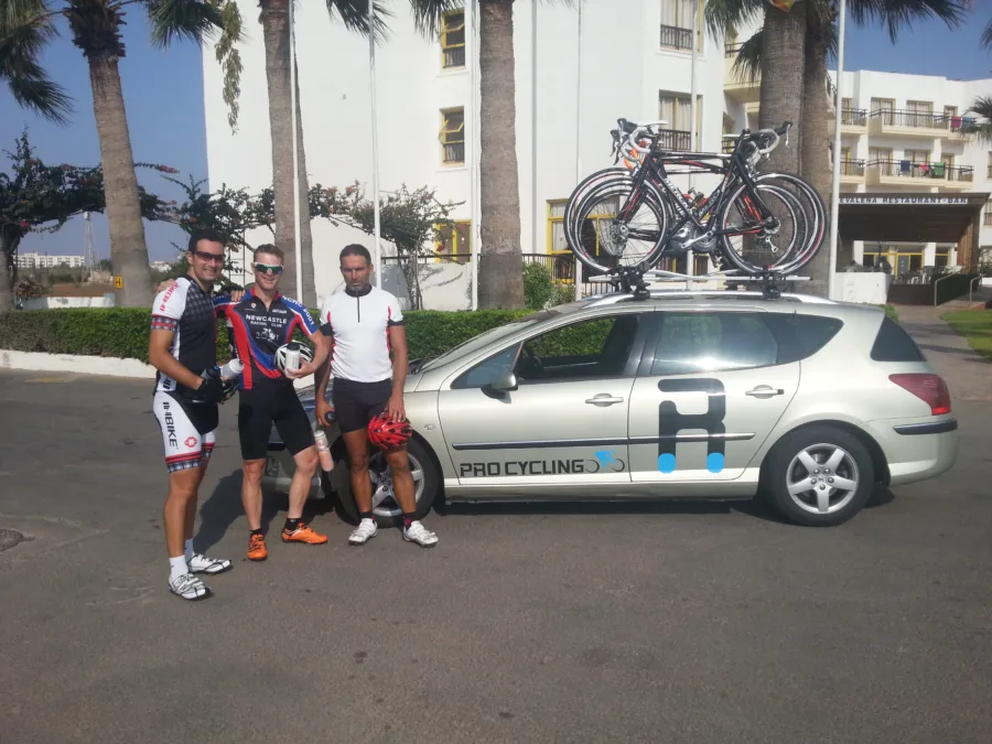 Riders and the team car outside a hotel, bikes on the roof rack