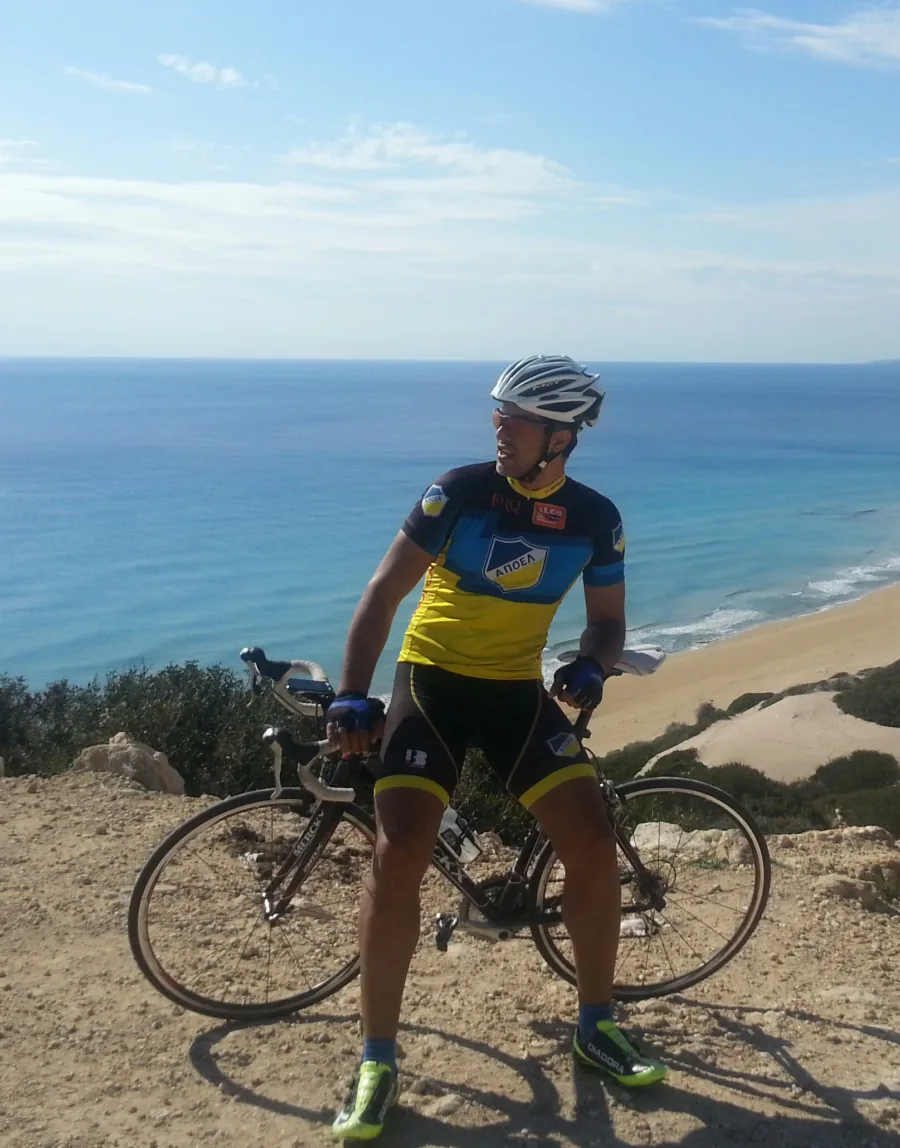 A rider standing over a road bike on a headland above a wide beach