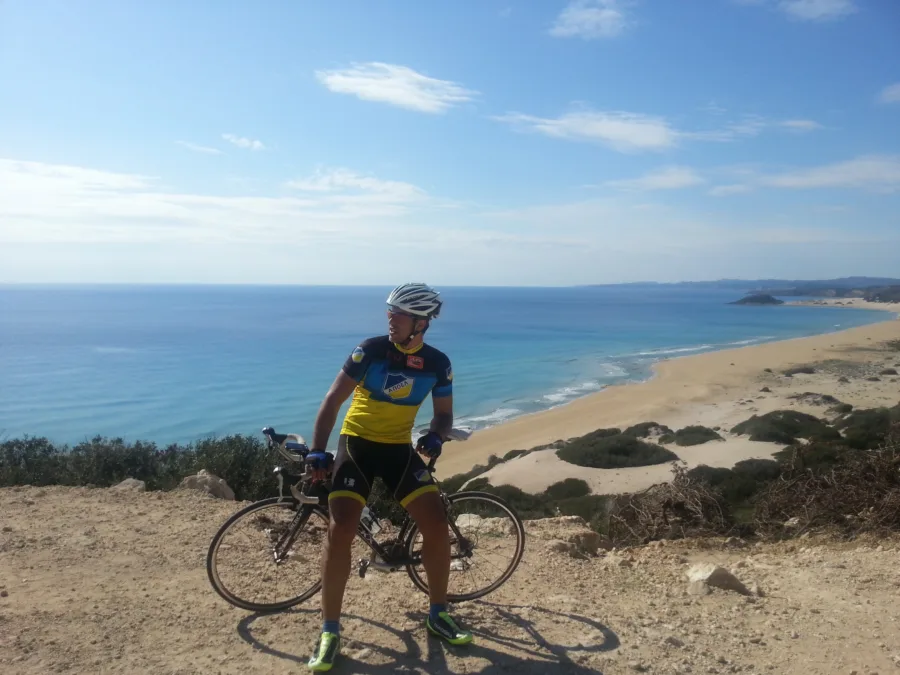 A rider in blue and yellow kit with a road bike above a long empty beach
