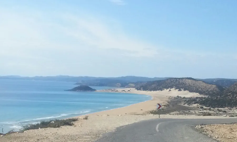 A wide sandy bay and headland seen from a track above it
