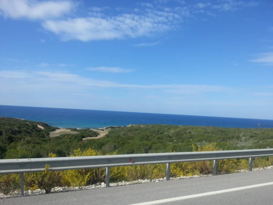 Scrubby green hillside dropping to a blue sea beside a coast road