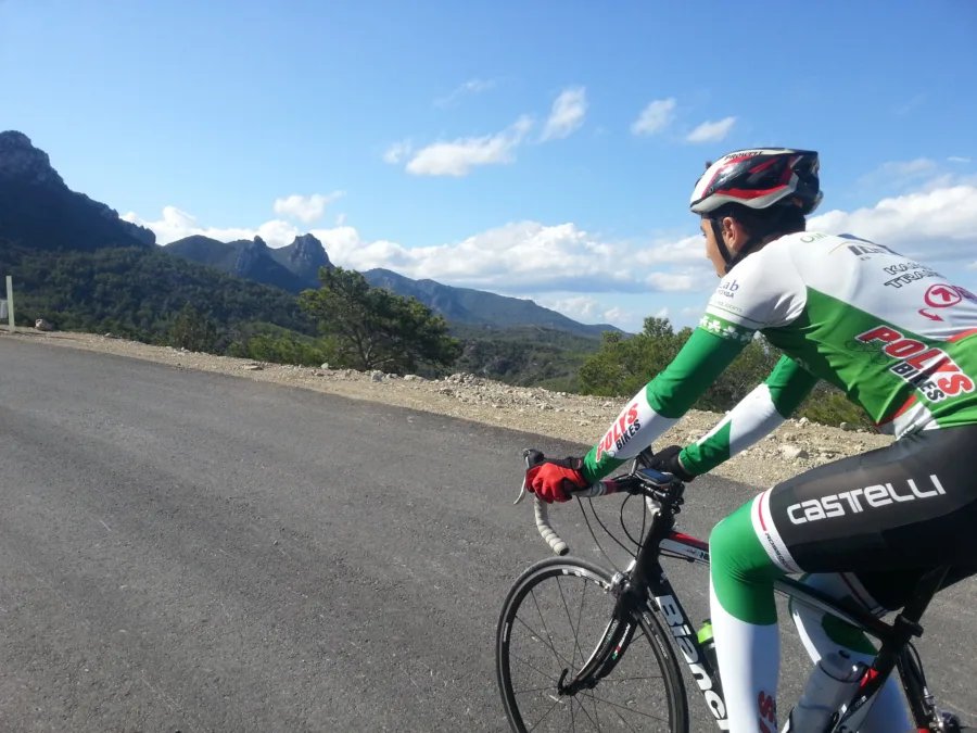 A rider in white kit on a road below a rocky crag