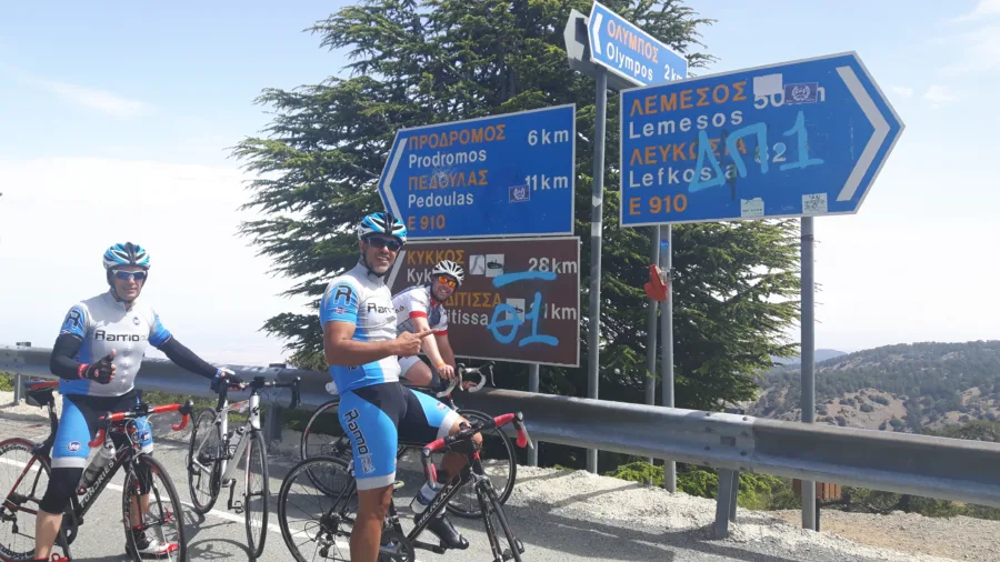 Two riders resting at a road junction beneath blue direction signs