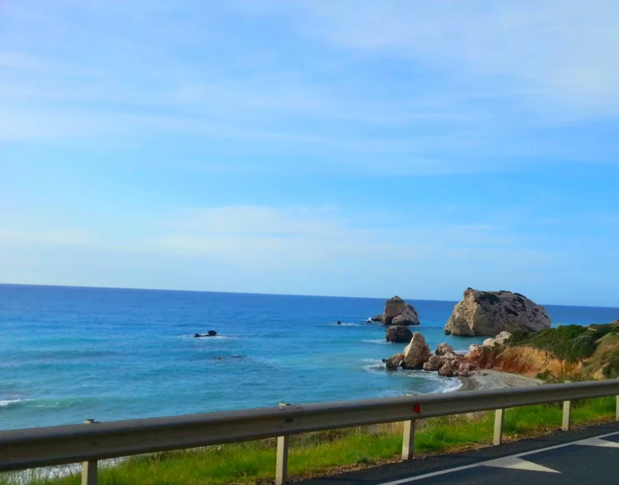 Sea stacks in clear turquoise water seen from a coast road behind a guardrail