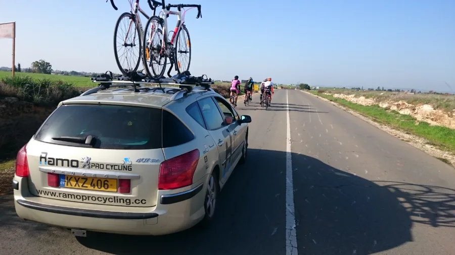 A Ramo Pro Cycling estate car with road bikes on the roof rack following a group of riders