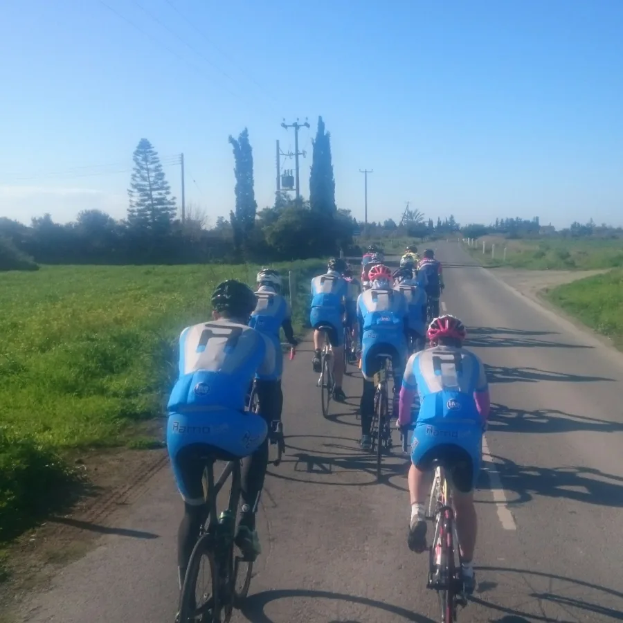 Riders in blue kit riding away down a road into low sun