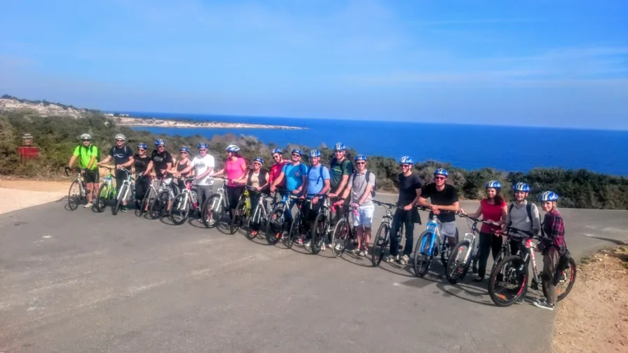 A long line of riders with their bikes on a track above the sea