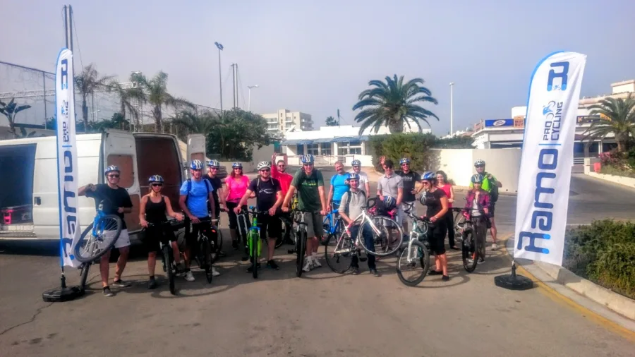 A large group with bikes beside a Ramo Pro Cycling flag and the van