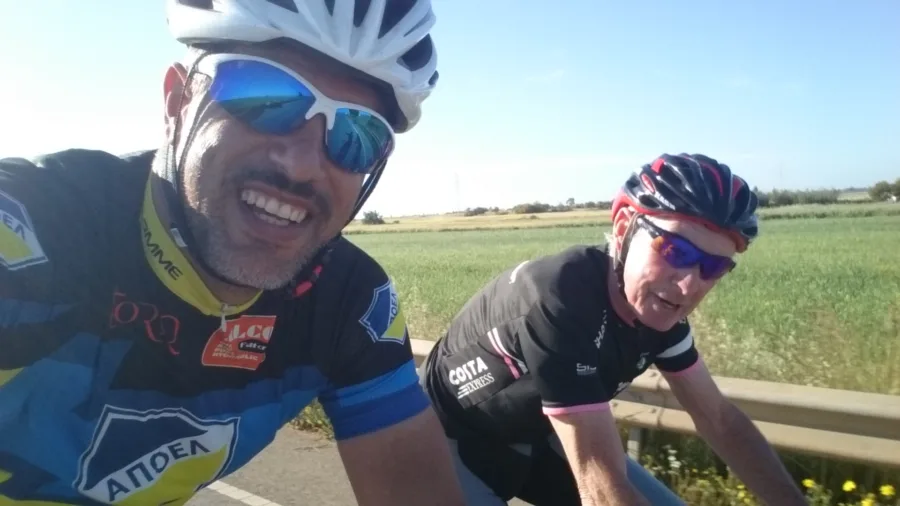A selfie of two riders laughing on a road beside green fields