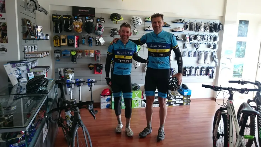 Two riders in matching kit standing among the bikes inside the shop