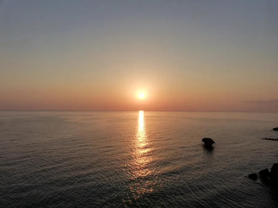The sun low over a calm sea, its light running straight to the shore