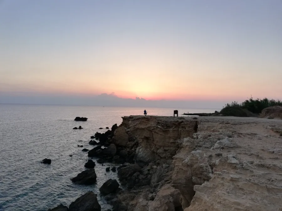 A rocky point above a calm sea with two figures standing on it
