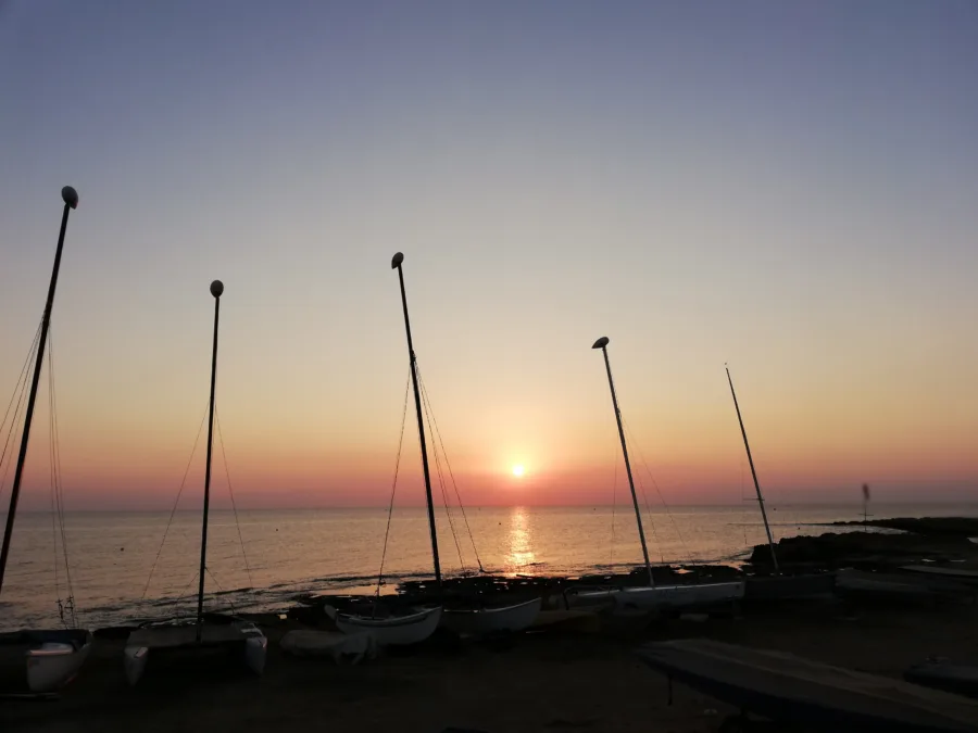 The sun rising behind the masts of dinghies drawn up on a beach