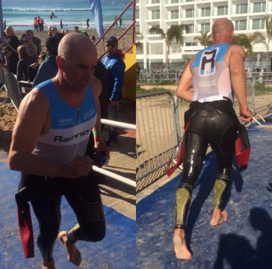 A triathlete running up the ramp from the swim and peeling off a wetsuit