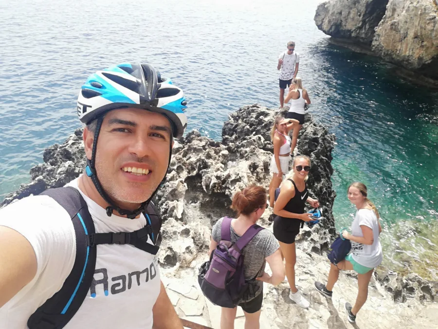 A selfie with a group at a rock arch above clear water