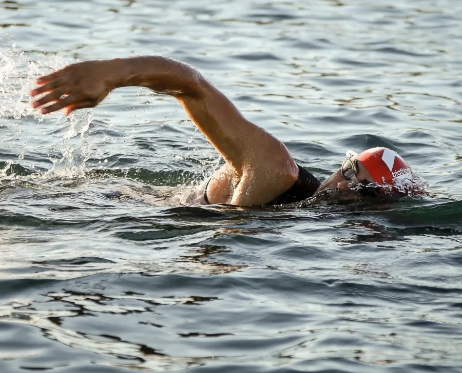 A swimmer mid-stroke in open water, one arm recovering above the surface