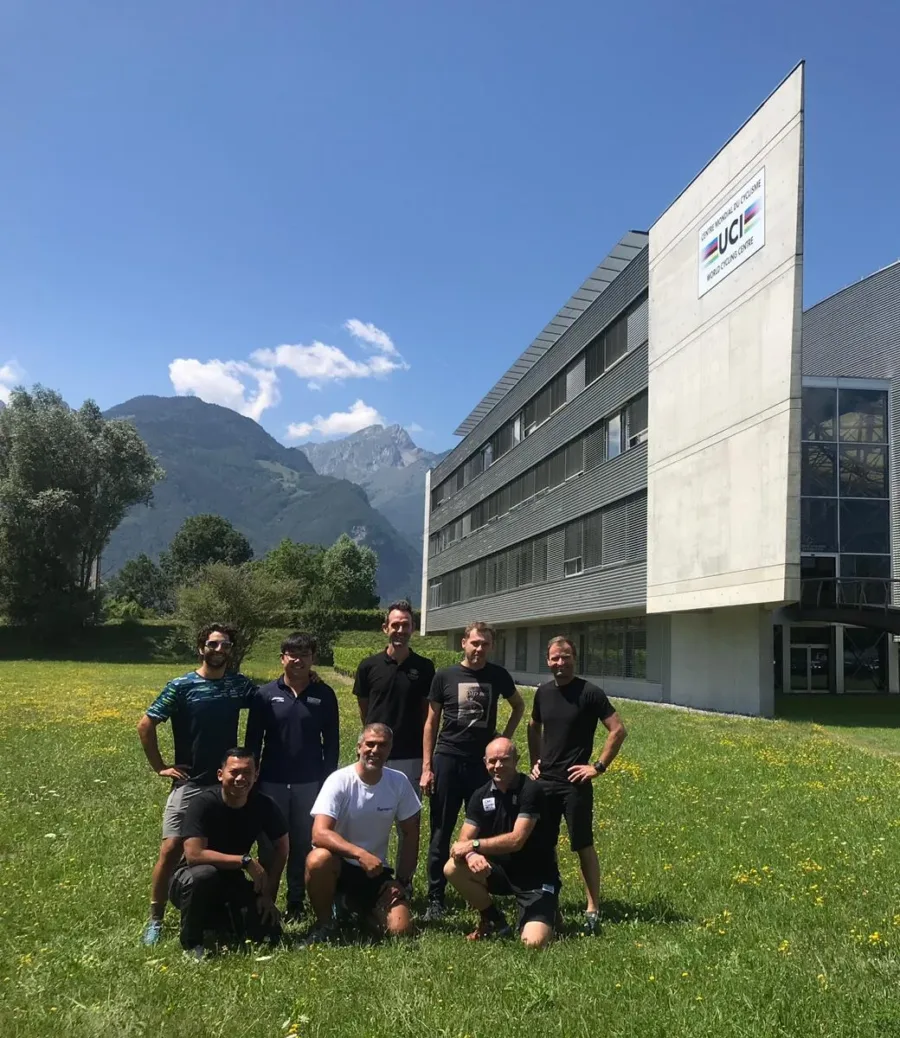 Eight coaches on the grass in front of the UCI World Cycling Centre, mountains behind