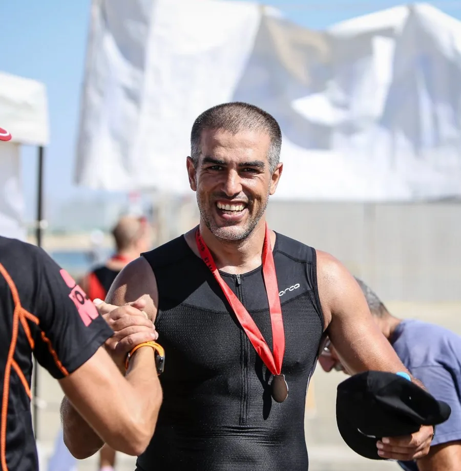 A man in a tri suit wearing a finisher medal, smiling at the finish